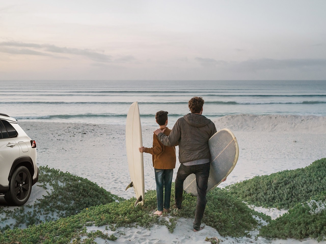 Ein Mann und ein Kind schauen auf den Horizont im Meer mit Surfboards in den Händen
