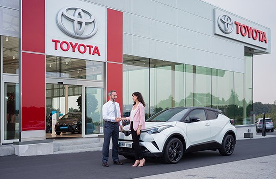 Händler schüttelt Frau vor einem Toyota Autohaus die Hand