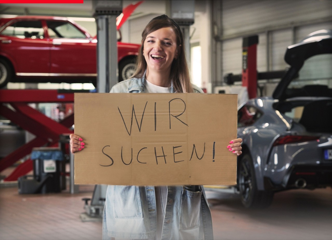 Person steht in einer Werkstatt und hält ein Schild in der Hand: Wir suchen!